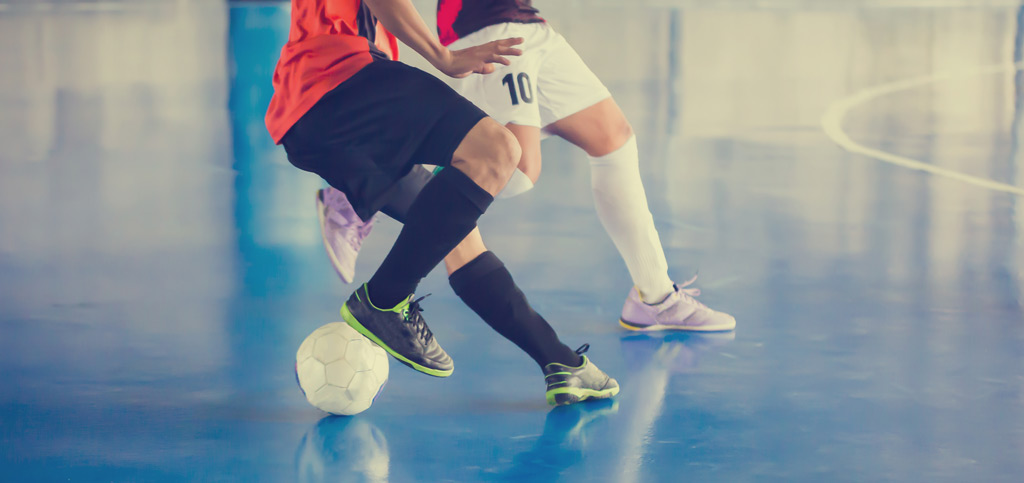 Unterkörper von zwei Fußballspielern beim Fußball Hallentraining, einer stoppt den Ball
